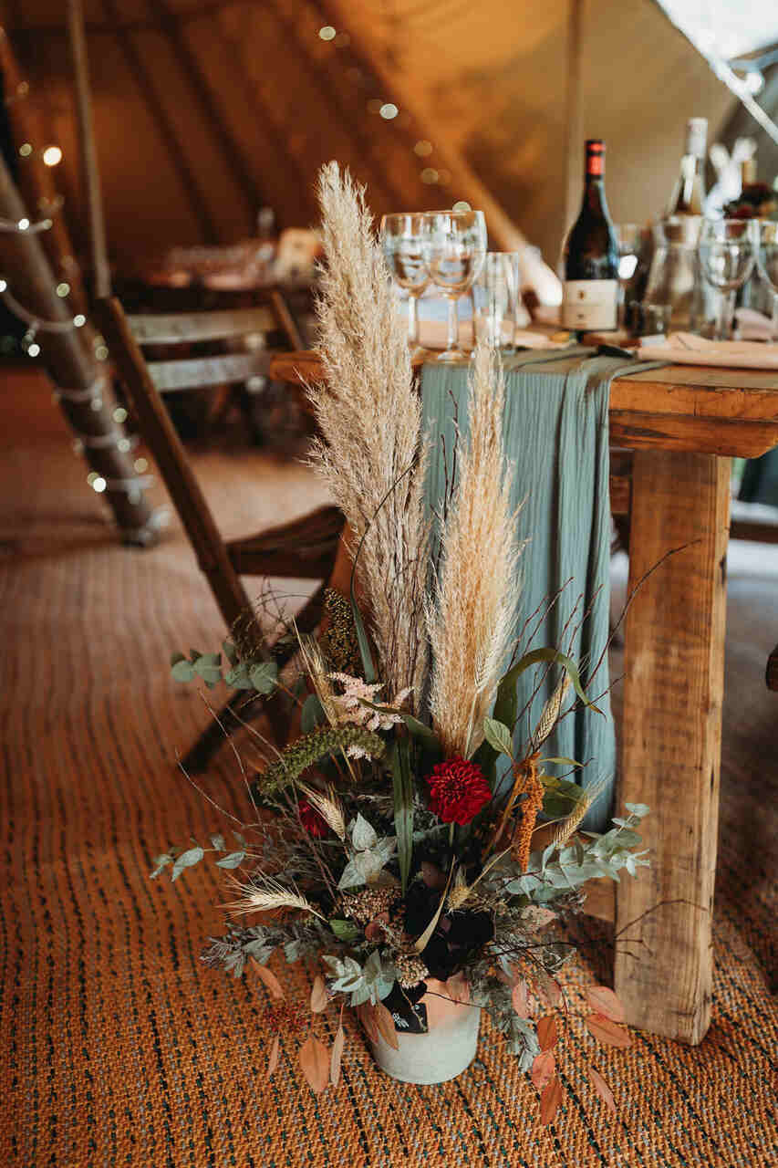 Arranjo de folhas e flores no chão, próximo ao pé da mesa dos convidados