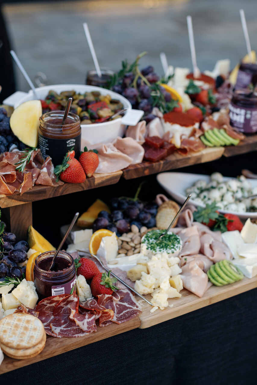 Uma mesa de buffet sofisticada com tábuas de queijos e embutidos, frutas frescas e condimentos artesanais