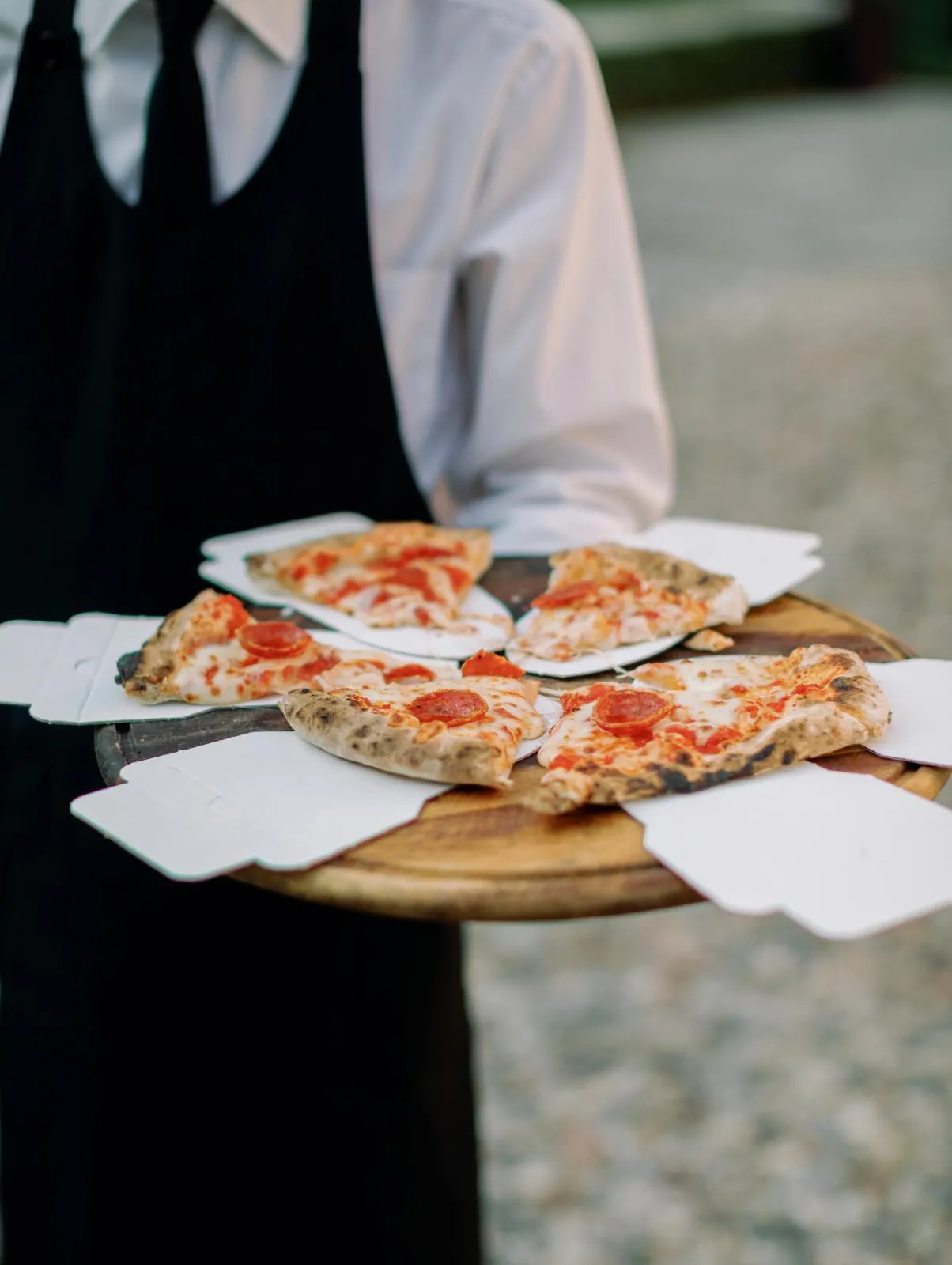 Garçom servindo fatias de pizza em um tabuleiro de madeira