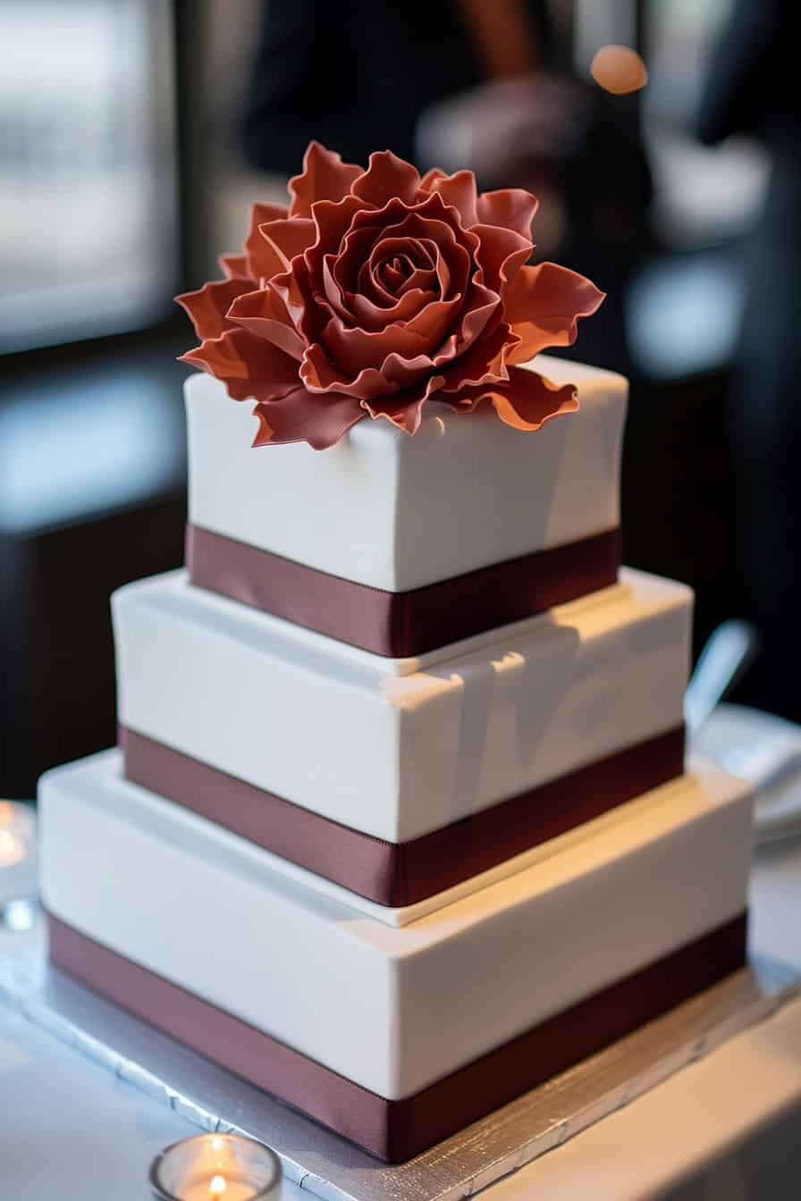 Bolo quadrado de 3 andares, branco com fitas marrons e no topo uma flor grande terracota