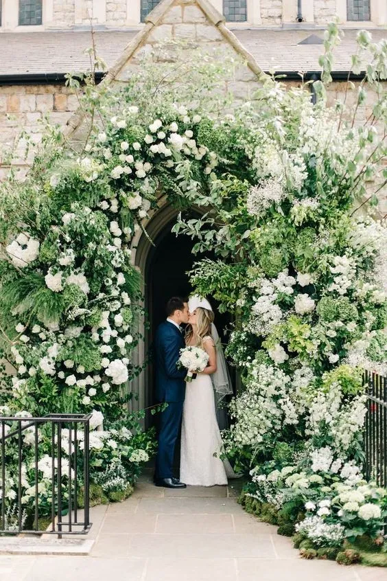 noivos se beijando em igreja com flores e plantas na porta