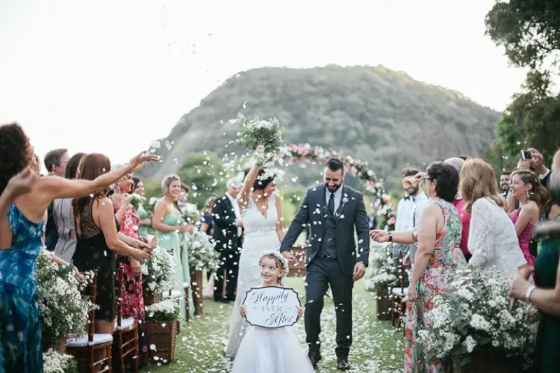 saída dos noivos na cerimônia de casamento ao ar livre com daminha levando uma plaquinha