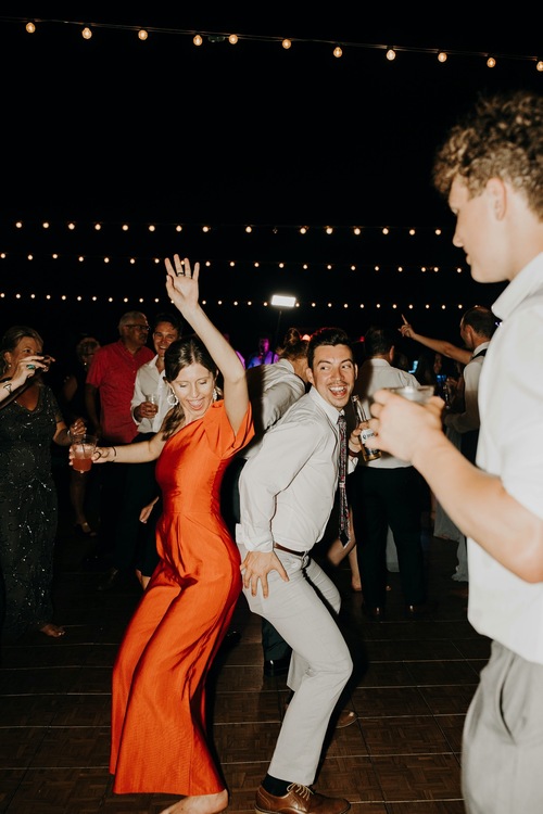 Convidados dançam e se divertem em uma pista de dança ao ar livre, com luzes ao fundo