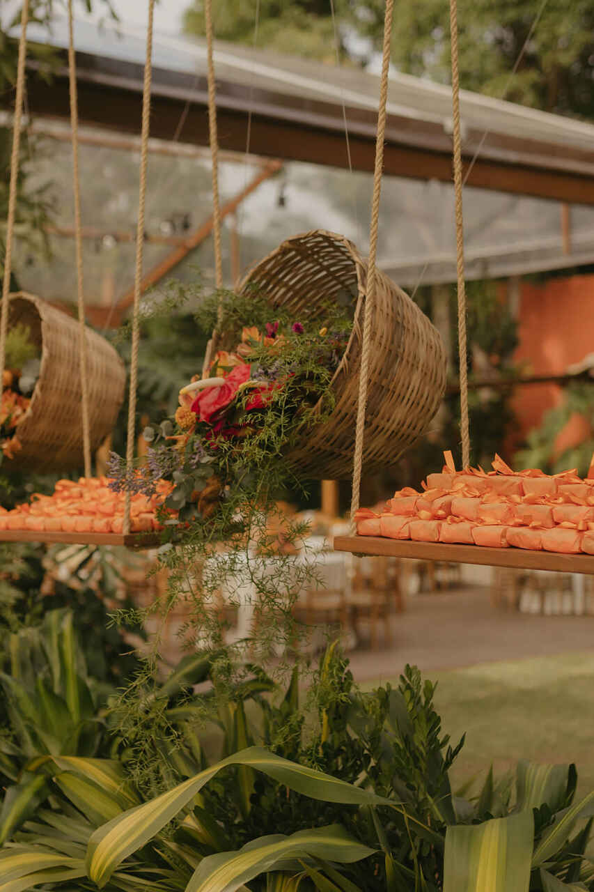 Decoração suspensa com cestas de palha recheadas de flores tropicais e doces em uma recepção ao ar livre