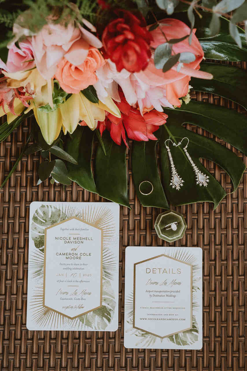 Convite de casamento tropical com detalhes em folhagem e flores exóticas, disposto em uma mesa com acessórios elegantes.