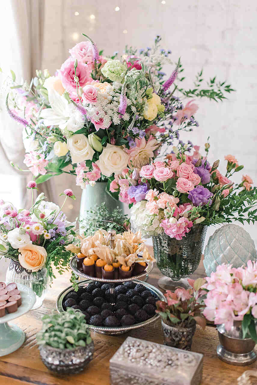 Uma mesa repleta de doces finos e arranjos florais exuberantes em tons suaves