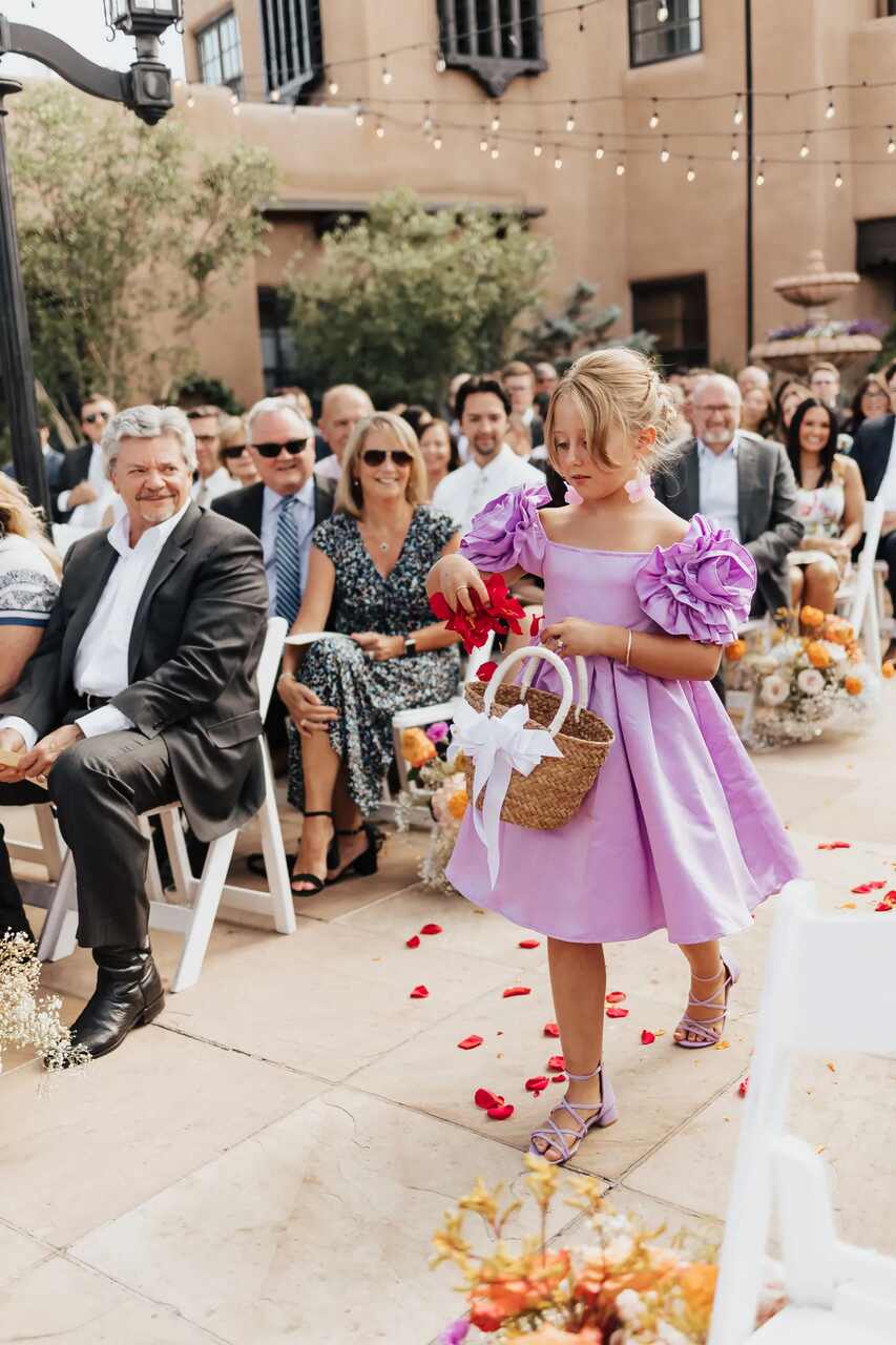 Uma florista com vestido lilás espalha pétalas pelo caminho