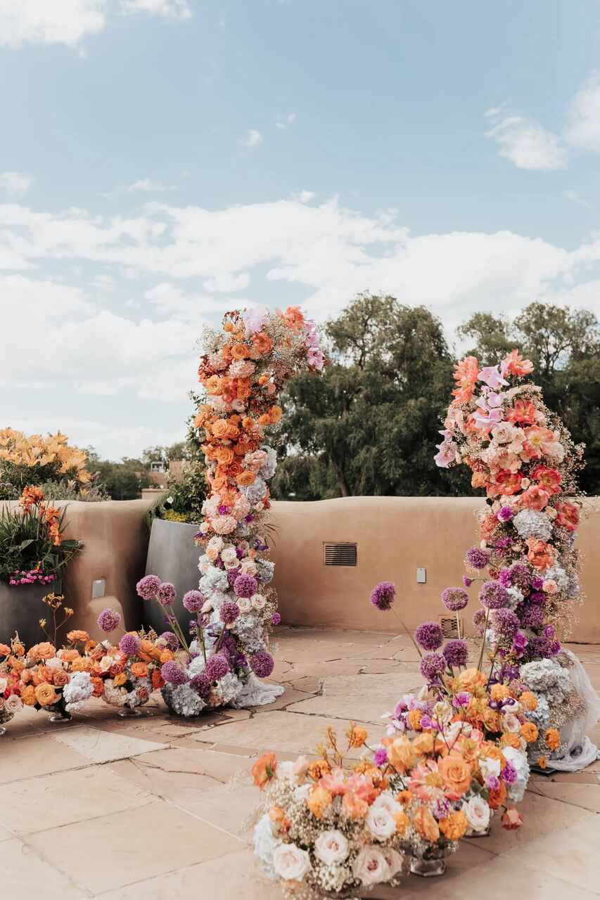 Um arco de flores vibrantes em tons alaranjados, roxos e brancos