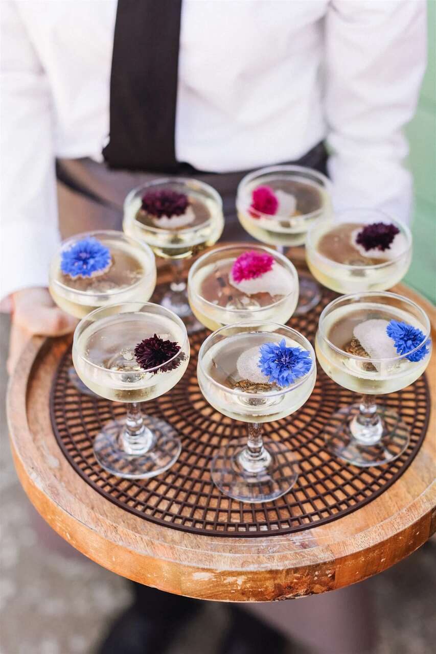 Taças de espumante com flores flutuantes sendo servidas em uma bandeja elegante.