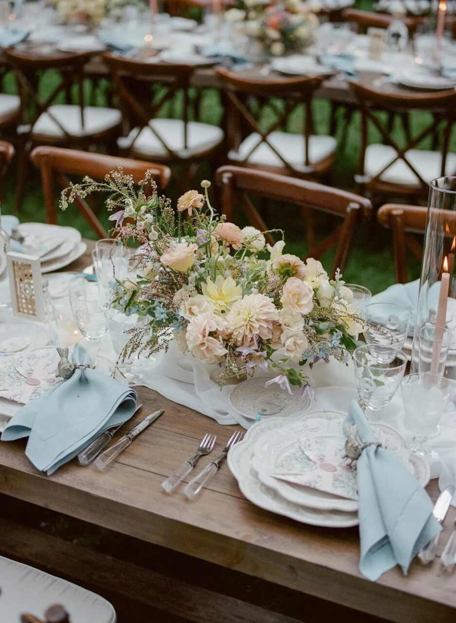 Uma mesa rústica e refinada, decorada com flores delicadas em tons pastel e louças clássicas