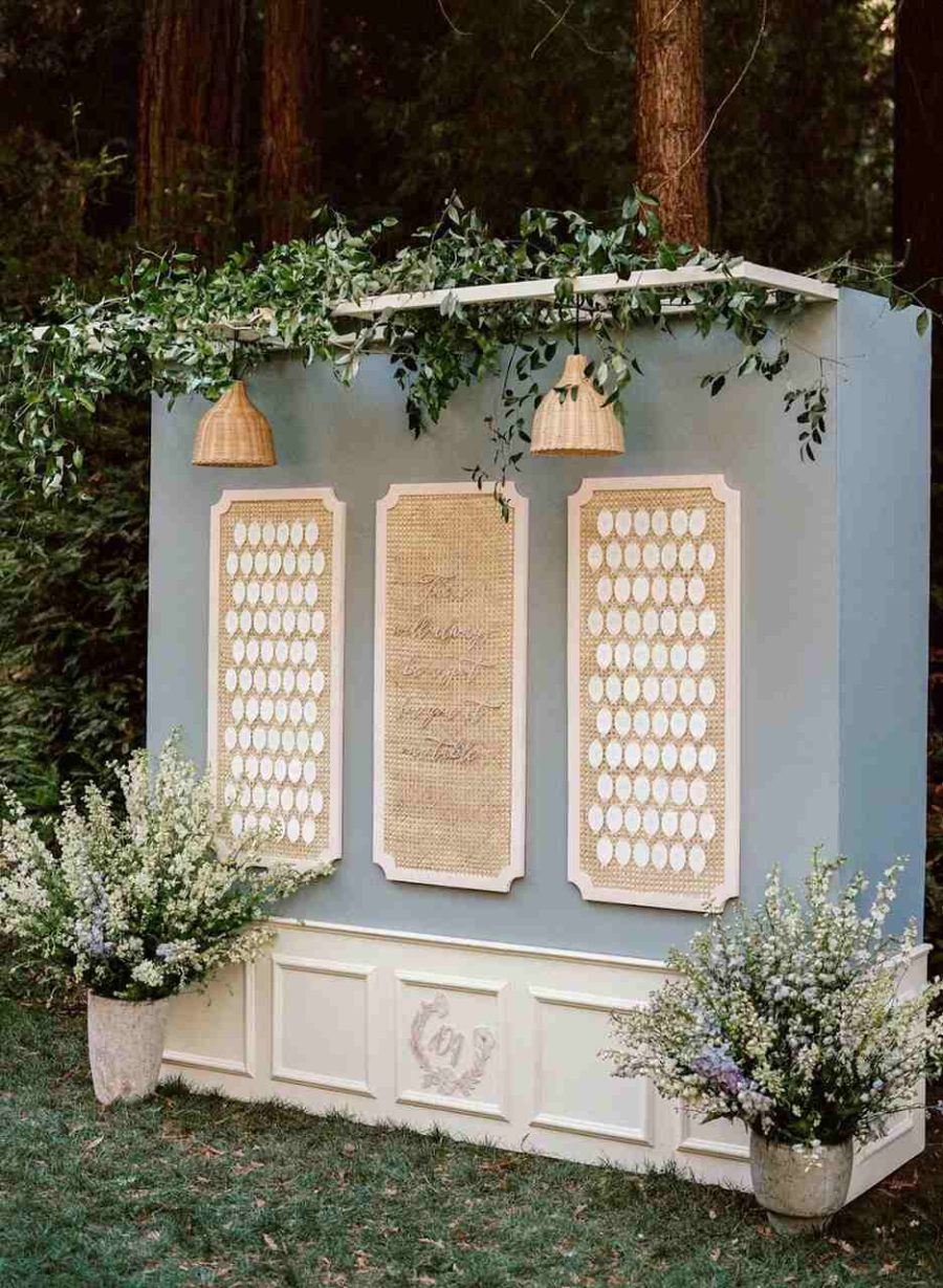 Um painel elegante com molduras delicadas, luzes pendentes e vasos repletos de flores brancas e lilases