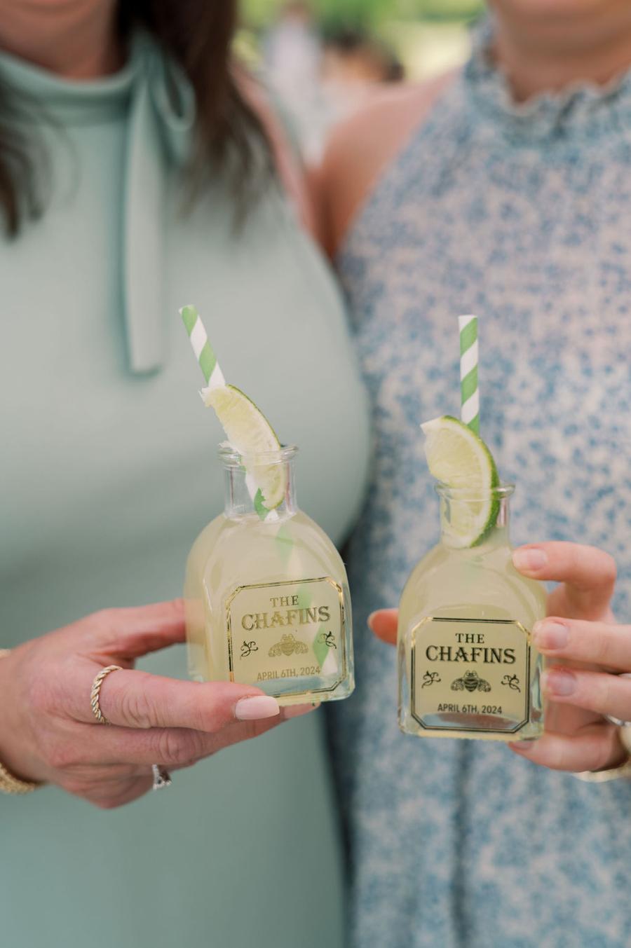 : Duas pessoas segurando garrafinhas personalizadas de limonada com rótulos delicados.