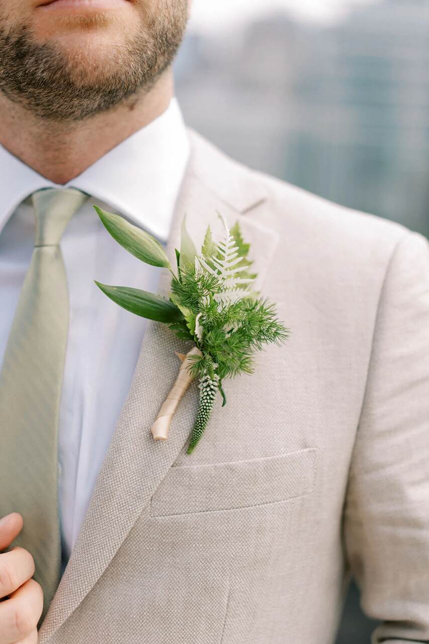 Terno claro com uma boutonnière verde minimalista, feita de folhagens naturais