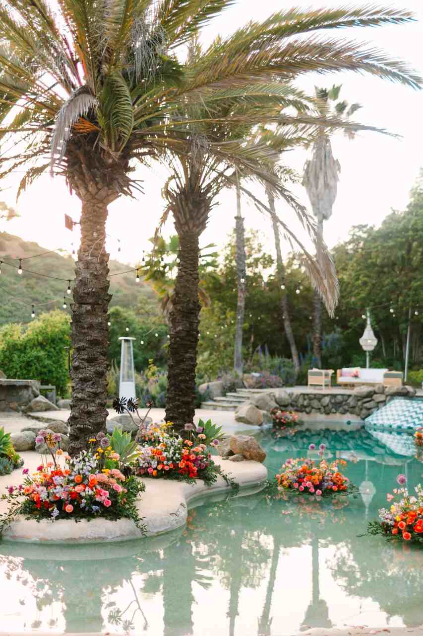 Paisagem tropical com palmeiras ao redor de uma piscina, decorada com arranjos florais coloridos