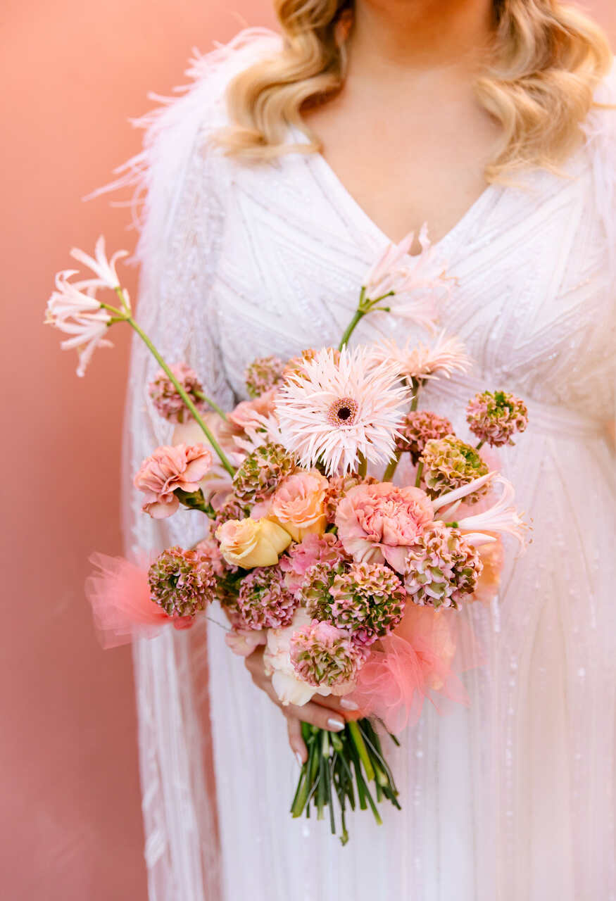 Uma noiva segura um delicado buquê em tons de rosa e pêssego, com flores variadas que trazem um toque romântico e moderno