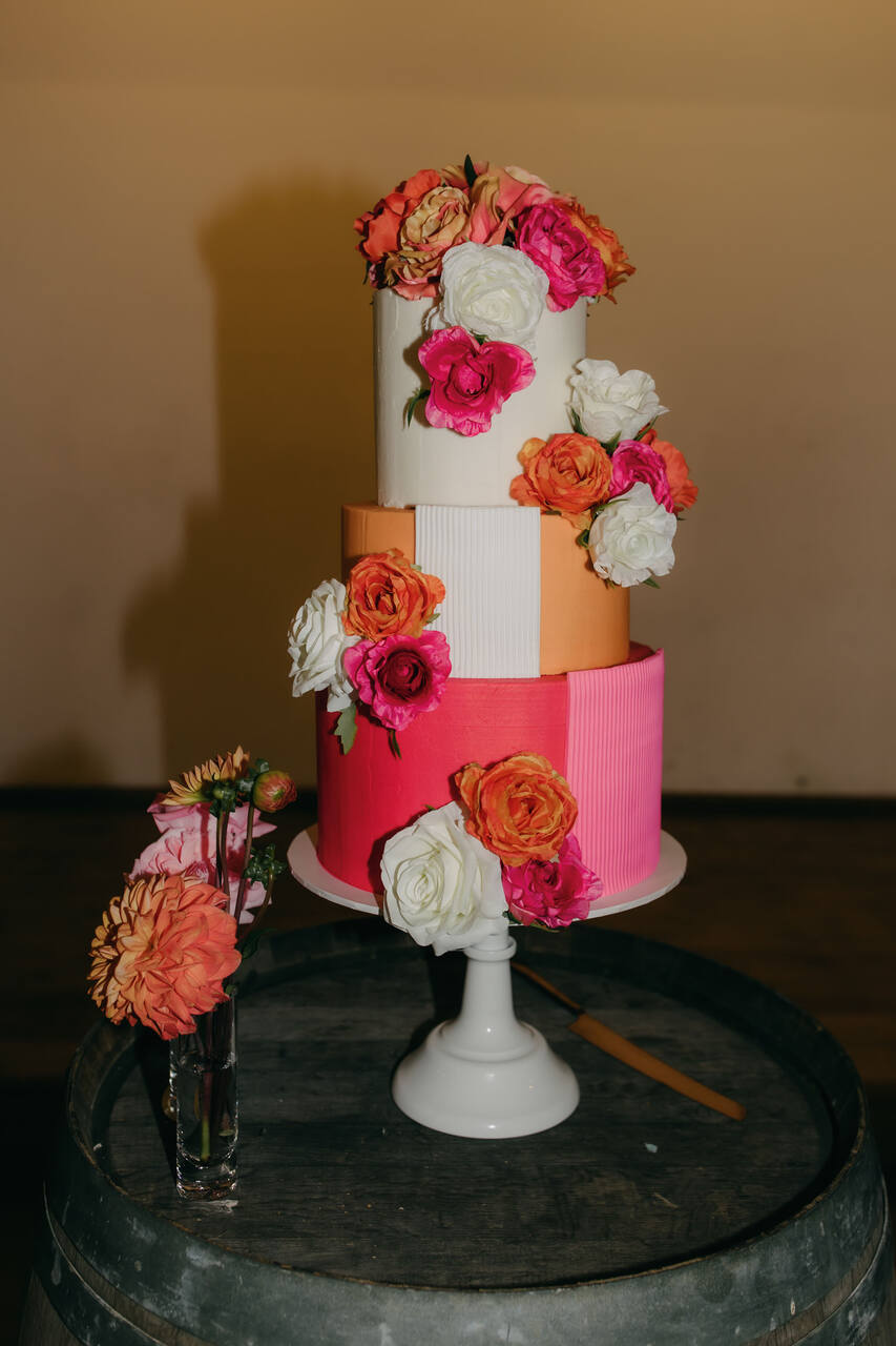 Bolo de três camadas em tons vibrantes, decorado com flores grandes em rosa, laranja e branco.