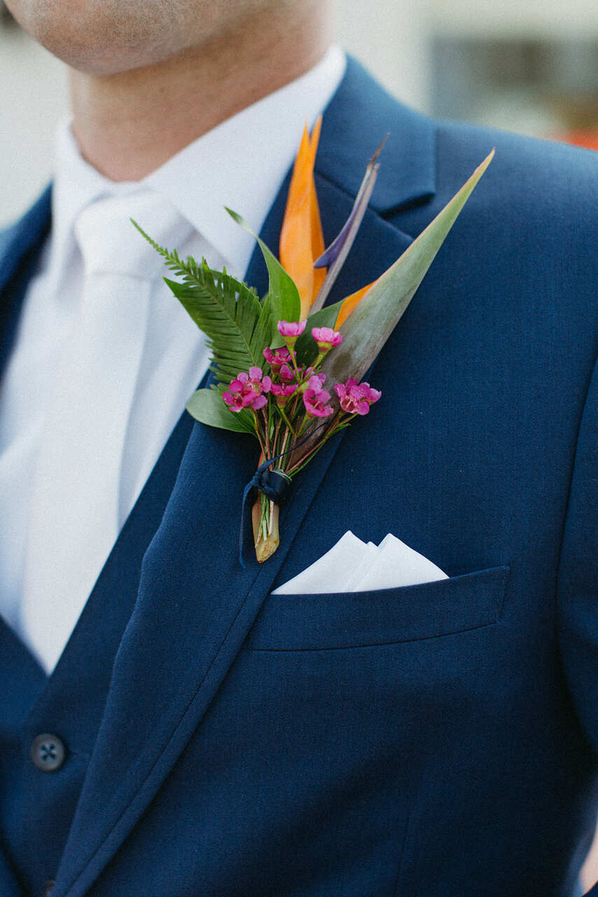 Um elegante terno azul com uma boutonnière composta por flores tropicais e folhagens