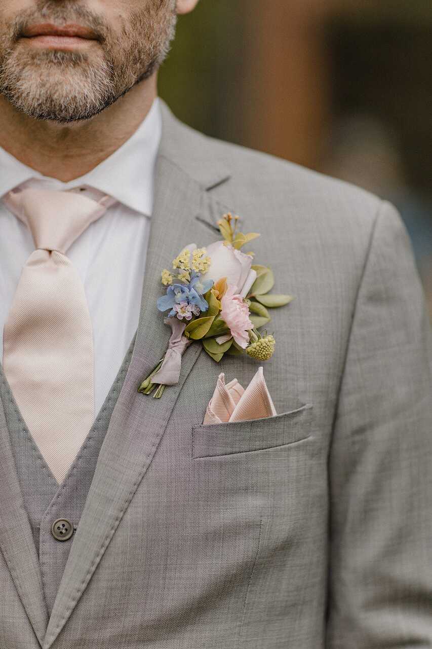 Close de um terno cinza com uma flor pastel elegante na lapela e lenço dobrado no bolso do paletó.