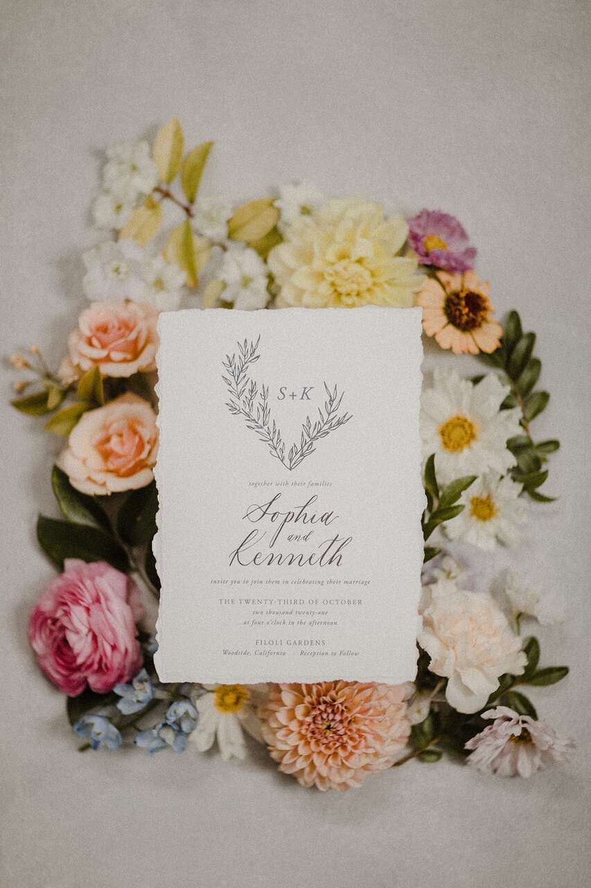 Convite de casamento com detalhes florais ao fundo, apresentando uma caligrafia sofisticada e um design clássico e romântico.