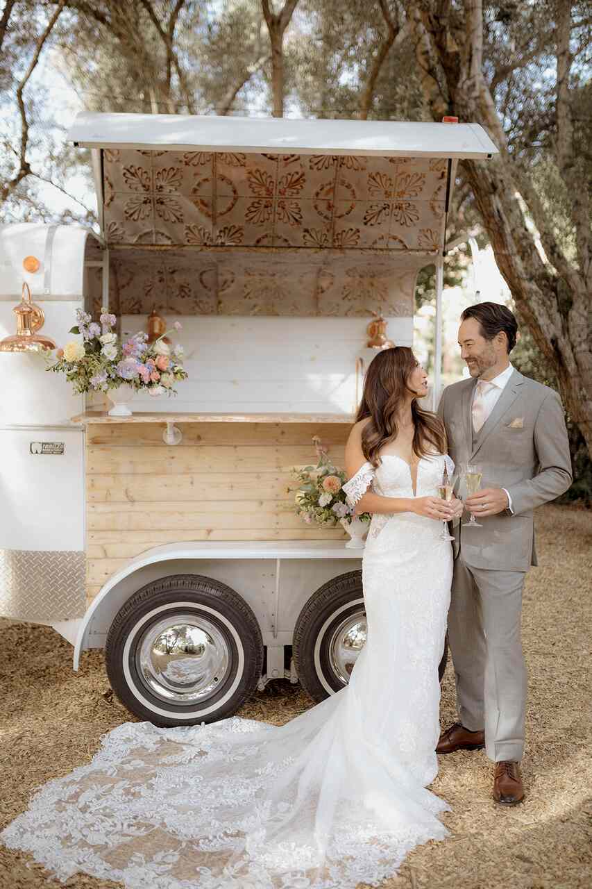 Um elegante trailer branco adaptado como bar de casamentos, adornado com flores e detalhes em madeira.