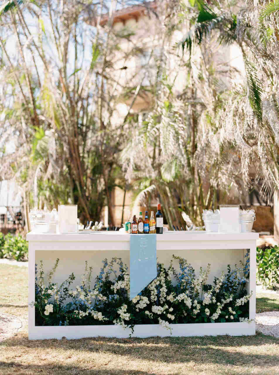 Um bar ao ar livre adornado com flores brancas e azuis, destacando a sofisticação em um cenário tropical.