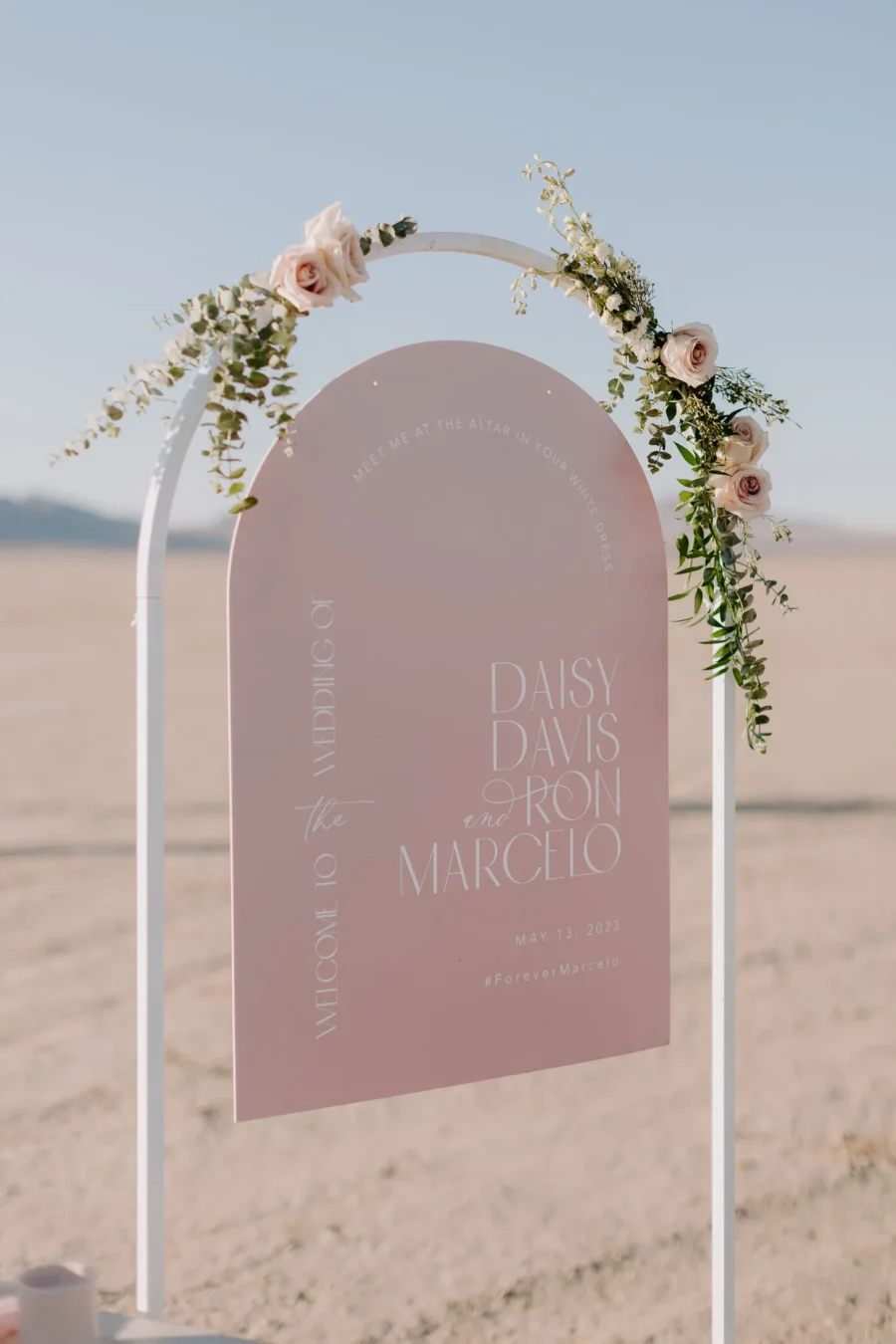 Placa rosa com flores suaves em arco, dando um toque romântico ao cenário desértico