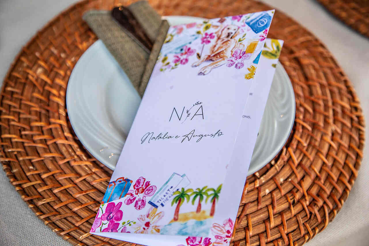 Cardápio personalizado com tema tropical sobre um prato branco, em uma mesa decorada com sousplat rústico e guardanapo neutro