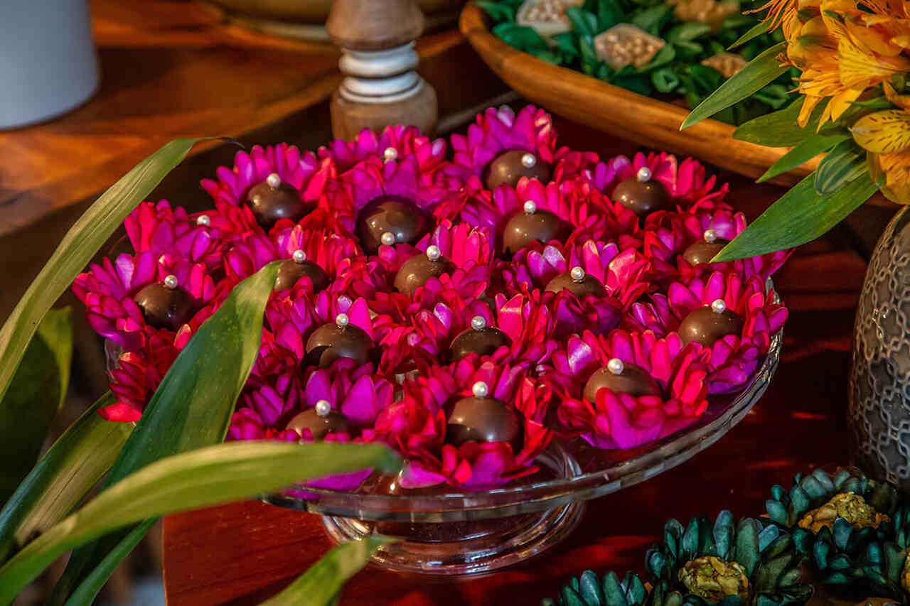 Docinhos decorativos em forma de flores vibrantes com detalhes de pérolas, dispostos em um prato de vidro