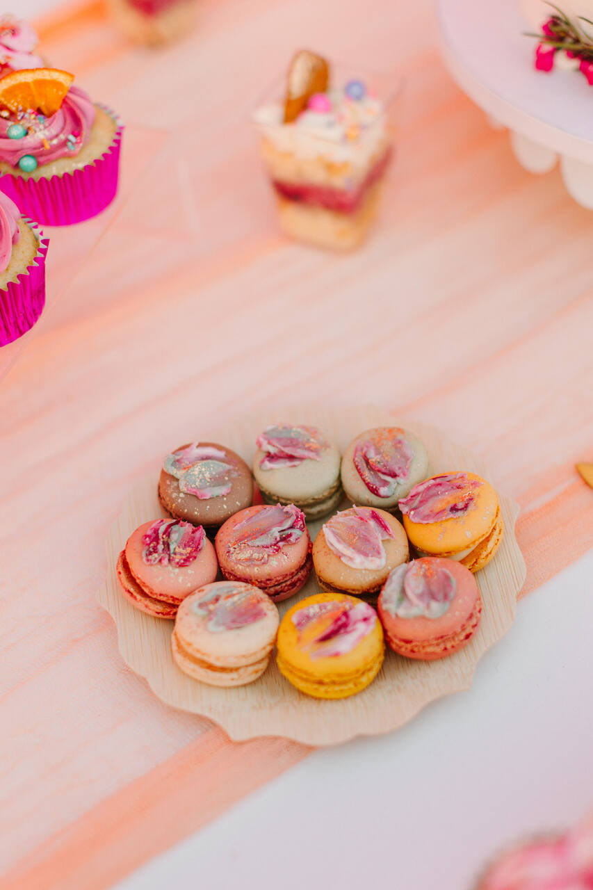 Prato com macarons decorados com cores pastel e detalhes brilhantes, em uma mesa de doces.