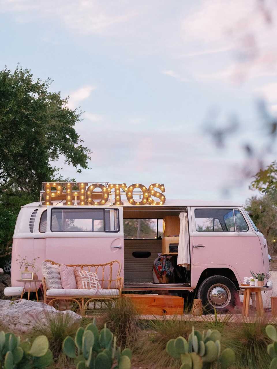 Uma charmosa Kombi rosa transformada em cabine fotográfica, decorada com luzes e almofadas, trazendo um toque retrô e aconchegante ao evento.