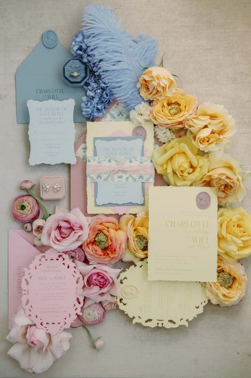 Convites de casamento elaborados em tons pastel cercados por flores amarelas e azuis