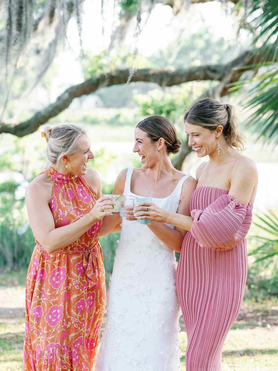 Noiva e amigas brindando alegremente em um casamento ao ar livre, todas vestindo roupas coloridas e descontraída