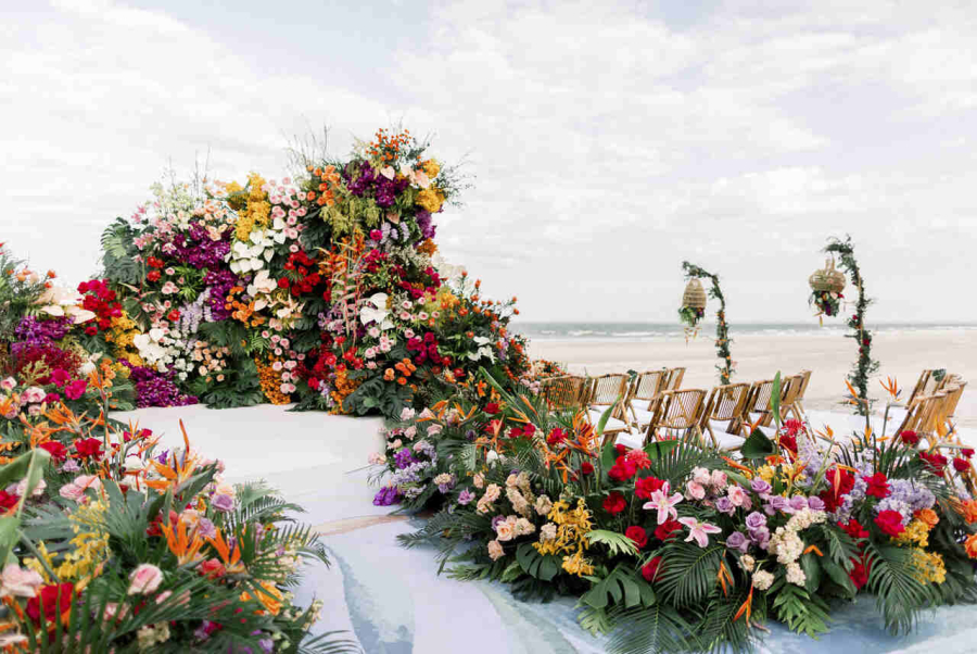 Palco de casamento decorado com um painel de flores tropicais vibrantes e arranjos exuberantes, com vista para a praia