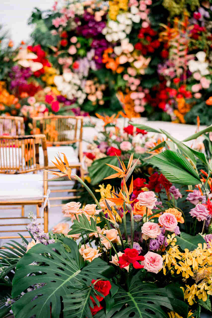 Área de cerimônia com cadeiras de bambu e uma decoração exuberante de flores tropicais e folhagens