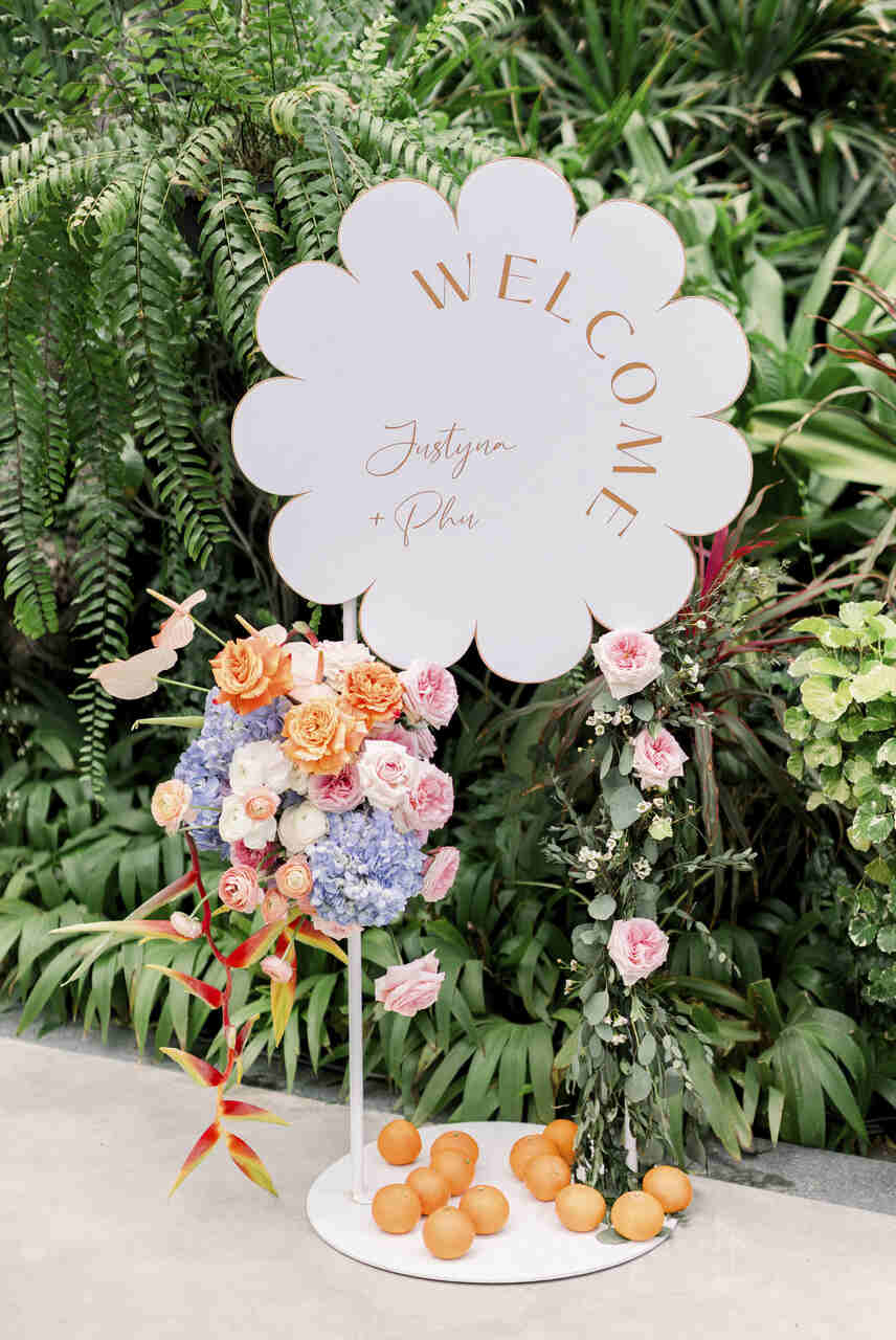 Placa de boas-vindas em formato de flor, decorada com arranjos florais coloridos e laranjas