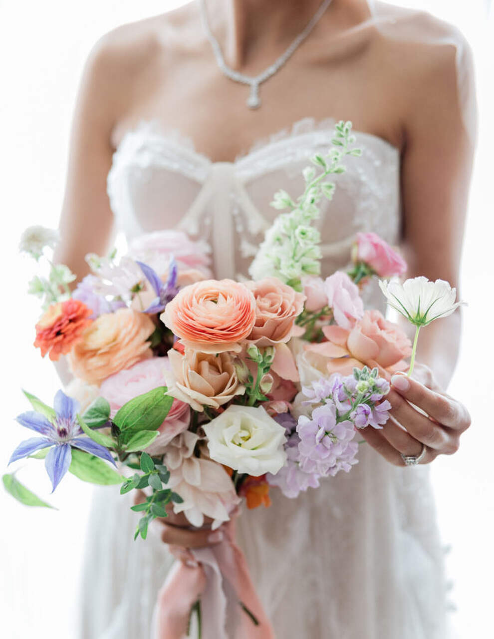 Uma noiva segura um buquê delicado com flores em tons pastel, como pêssego, lavanda e branco,