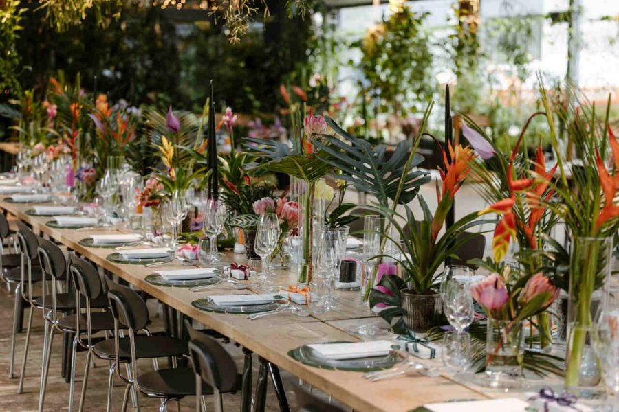 Mesa comprida decorada com flores tropicais e arranjos modernos em um ambiente repleto de verde.