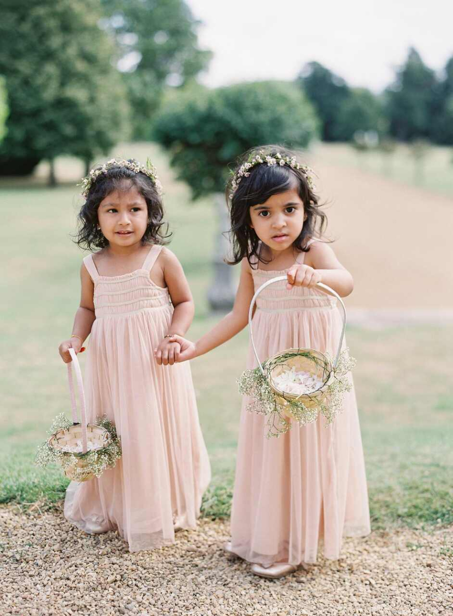 Duas pequenas daminhas em vestidos de tule bege seguram delicados cestos de flores