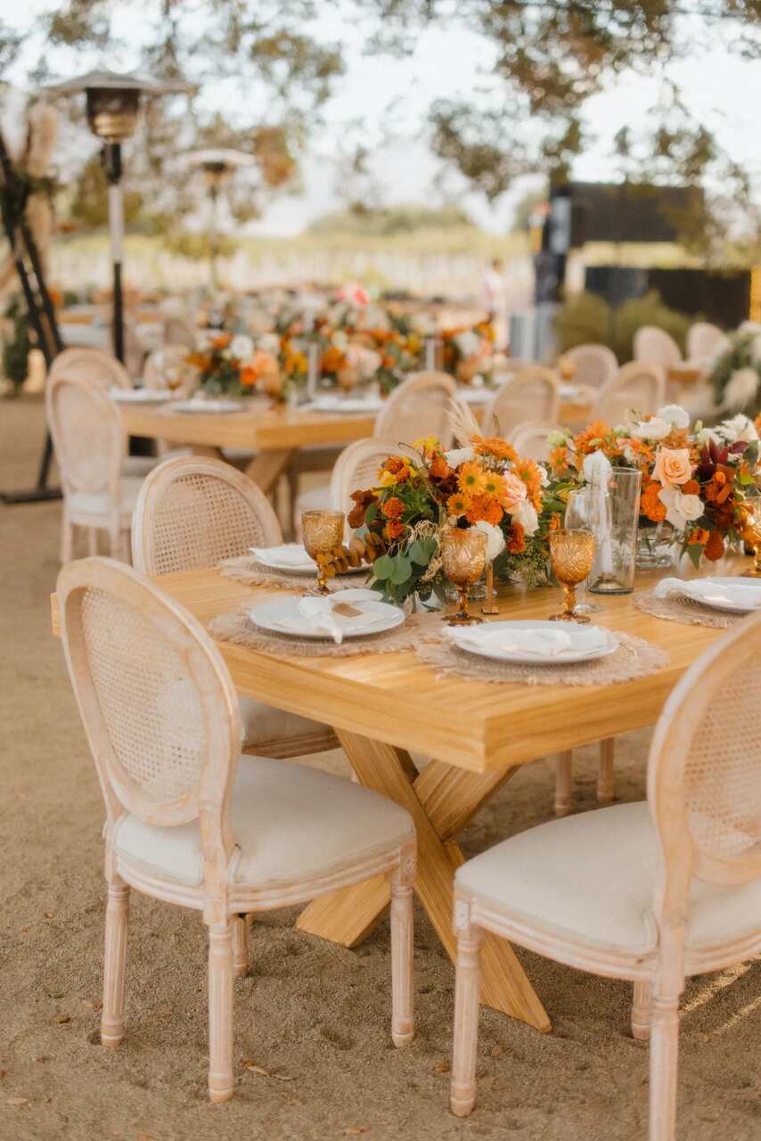 Mesas ao ar livre com cadeiras clássicas e decoração floral em tons quentes