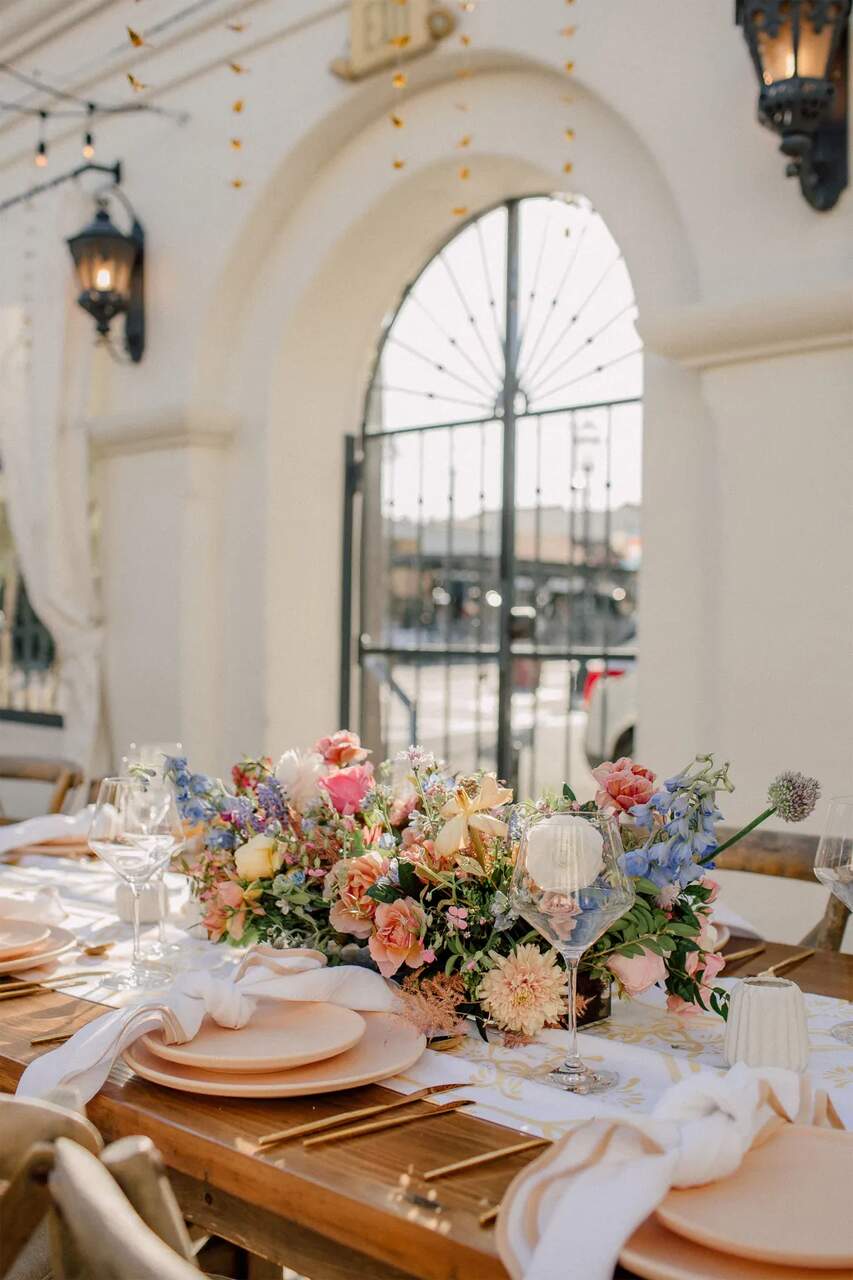 Uma mesa charmosa com arranjos florais coloridos, louças elegantes e um ambiente iluminado pela luz natural