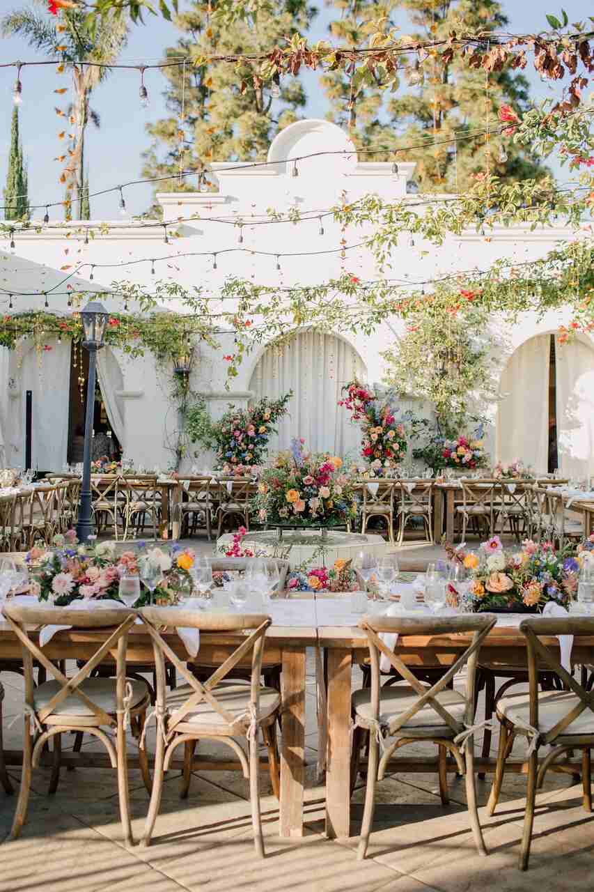 Uma elegante montagem ao ar livre com mesas rústicas decoradas com flores vibrantes e guirlandas de luz