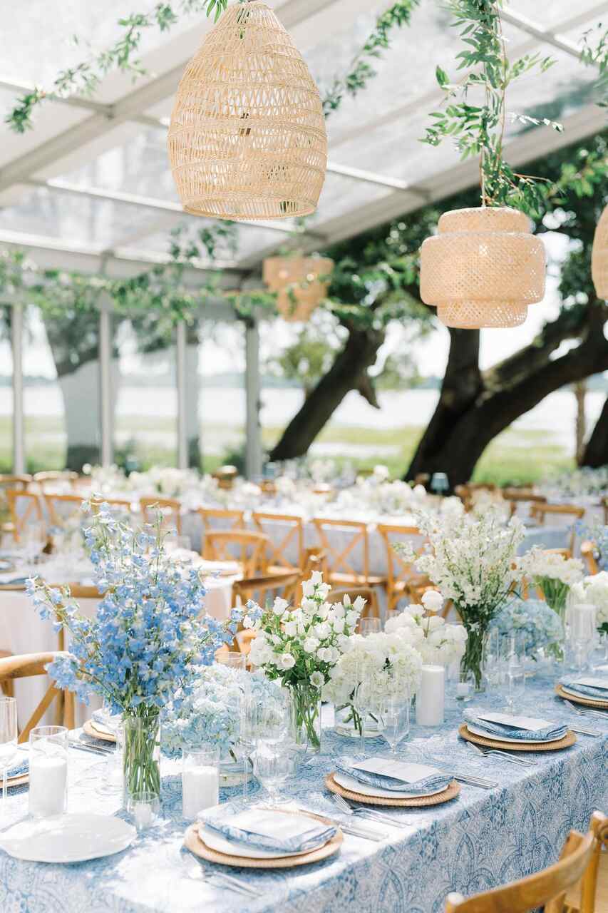 Um espaço ao ar livre com mesas elegantemente decoradas, luzes suspensas e uma paleta em azul e branco