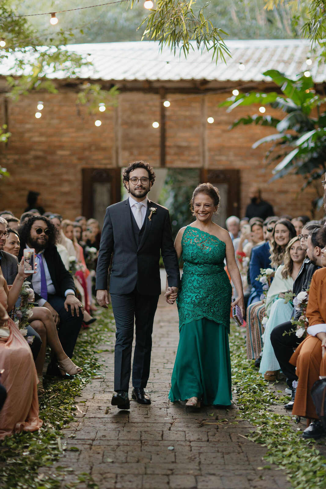 entrada do noivo com terno cinza escuro com a mãe com vestido verde