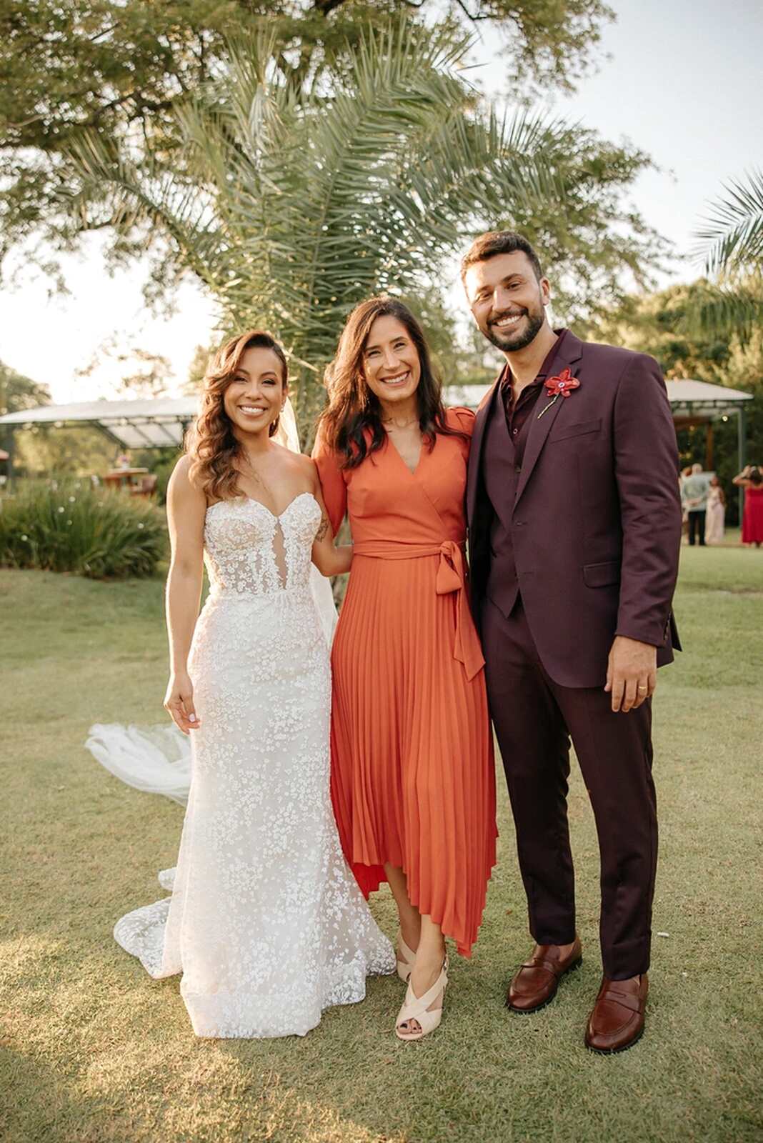 noivos ao lado de convidada com vestido laranja