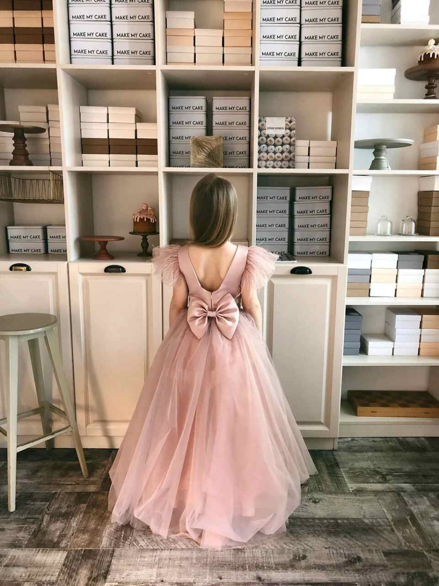 Uma garotinha de costas, vestida com um vestido rosa com um grande laço na cintura