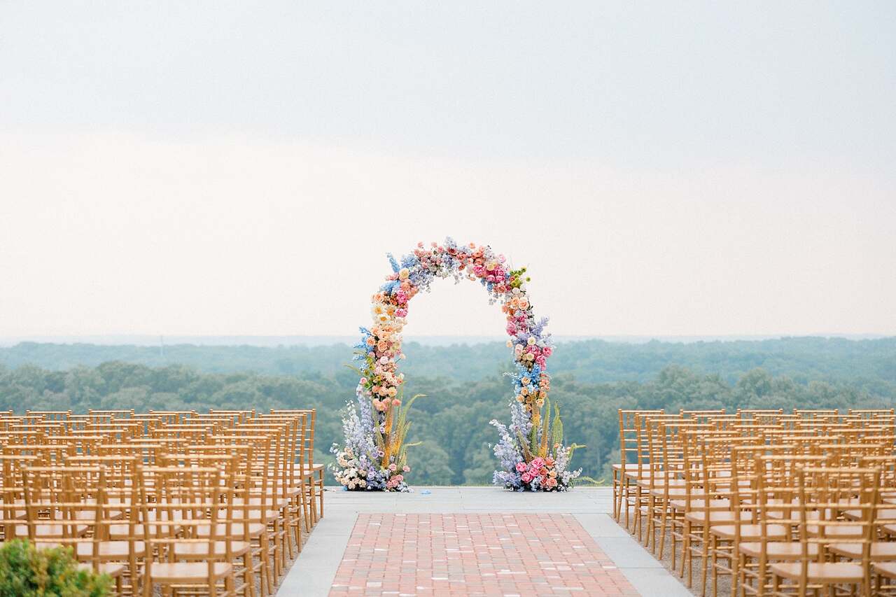 Um arco floral deslumbrante com flores coloridas em um cenário ao ar livre, rodeado por cadeiras douradas