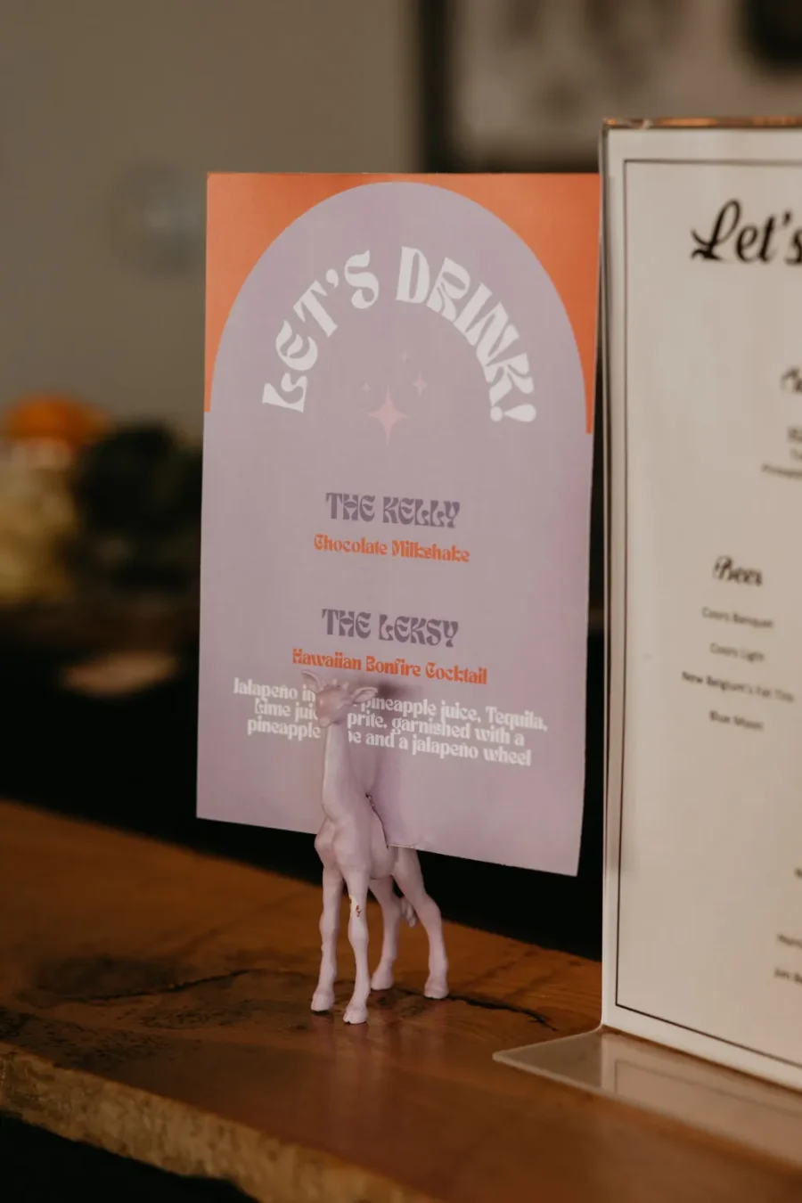 Menu de bebidas de casamento com design moderno, apresentando opções de coquetéis e milkshakes, com uma ilustração divertida de um unicórnio como apoio.