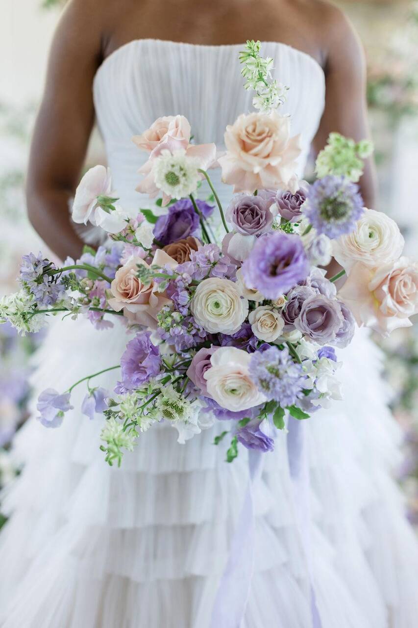 Noiva segurando buquê de rosas lilases, pêssegos e flores brancas, em vestido de tule branco.