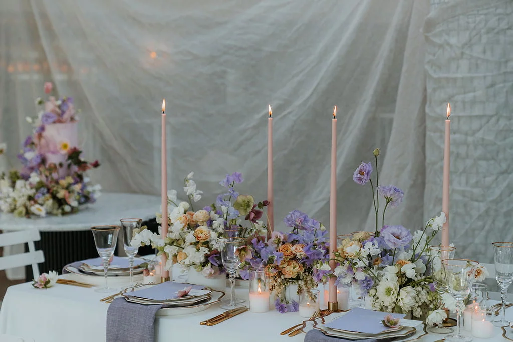 Mesa de casamento decorada com velas altas e arranjo floral em tons de lilás e rosa