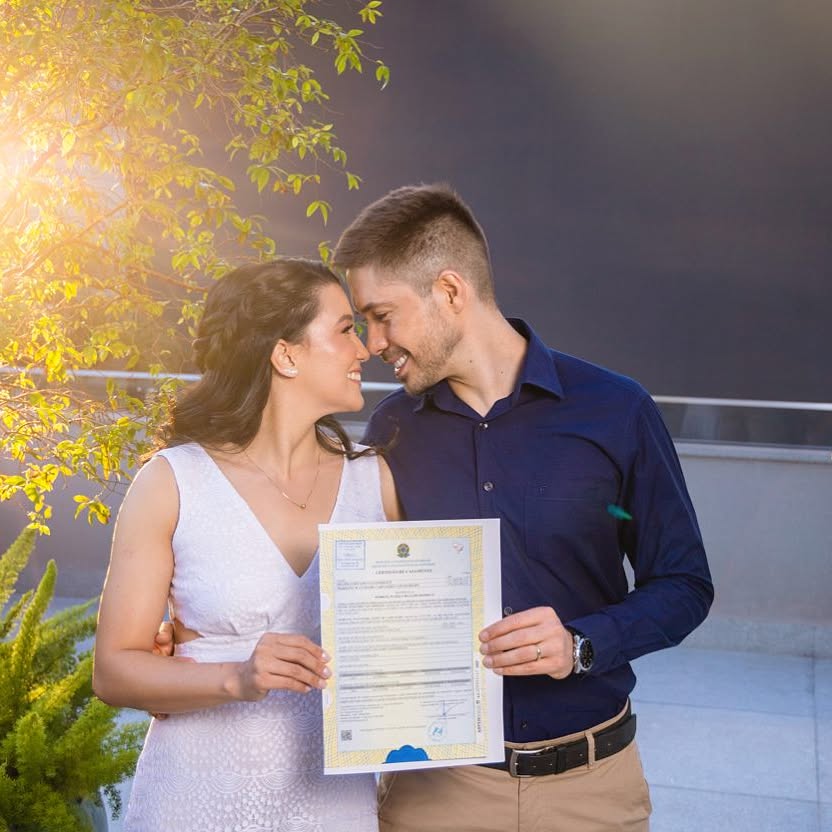 Casal sorridente em um momento de felicidade ao ar livre, segurando a certidão de casamento e compartilhando um olhar apaixonado 